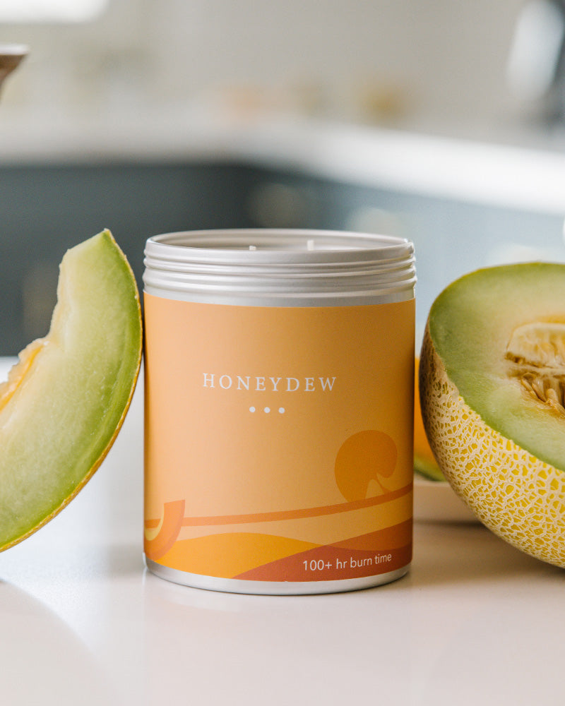 A Large Orange Tin With Melon Designs on the side. Made in Kalamazoo, MI. Scented with Melons, Honey, and Earth.