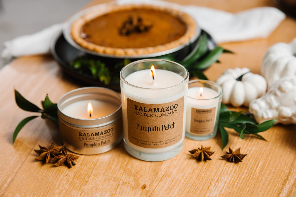 A set of three pumpkin candles in front of a pumpkin pie
