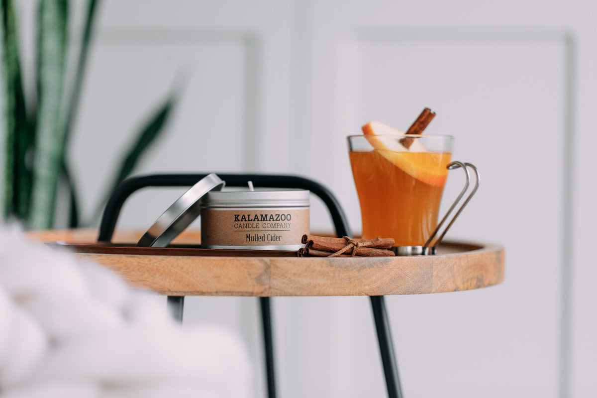A mulled cider candle tin next to a glass of cider